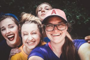 Smiling young woman taking selfie of herself and 3 friends