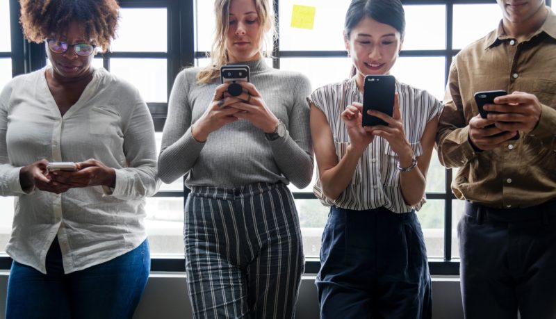 4 women standing and looking at smartphone